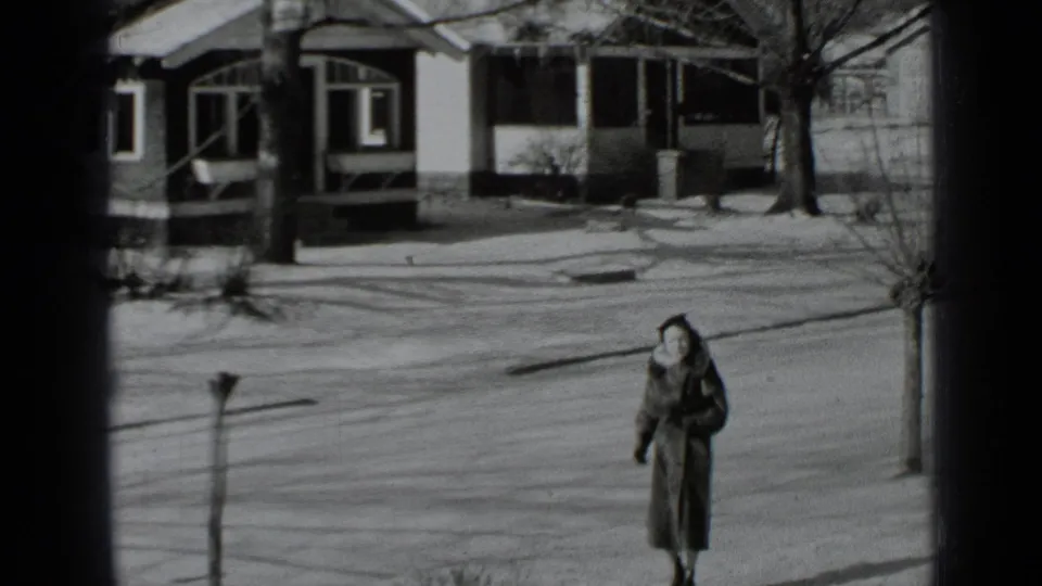 A bundled woman in a long coat walks along a snow-dusted residential sidewalk in New York, 1939.