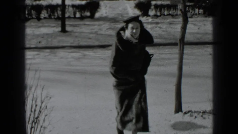 Near the end of the clip, the woman is closer to the camera, bundled in a dark winter coat beside a snow-lined street.