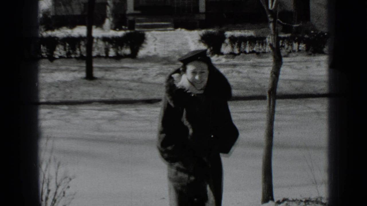 Woman in a winter coat walks along a snowy sidewalk toward the camera.