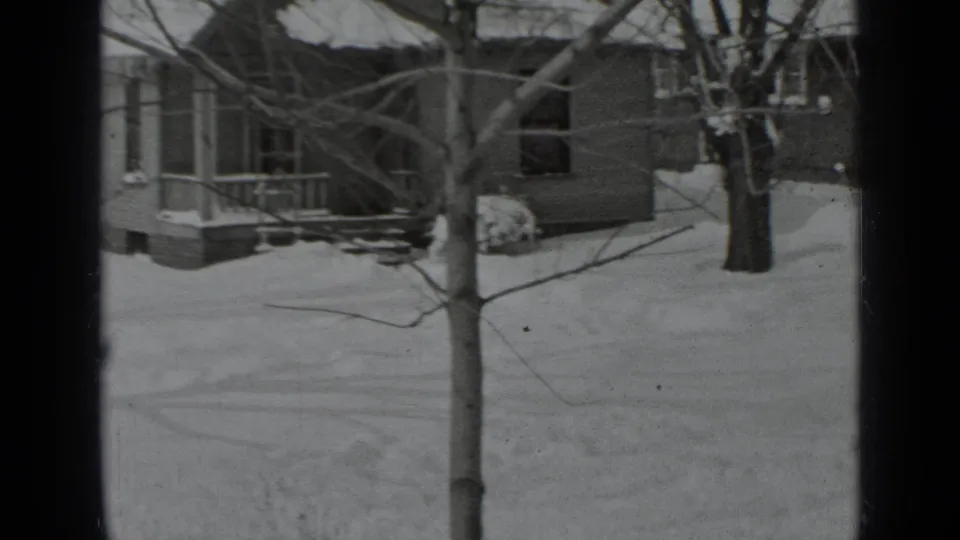 1939 New York winter home-movie view of a house, snow-covered ground, and bare trees framed by a dark interior window edge.