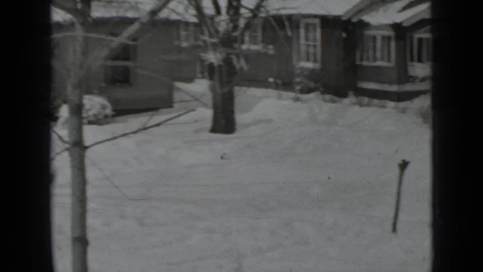 1939 New York home-movie view of snowy houses, bare trees, and deep winter ground cover seen from indoors.