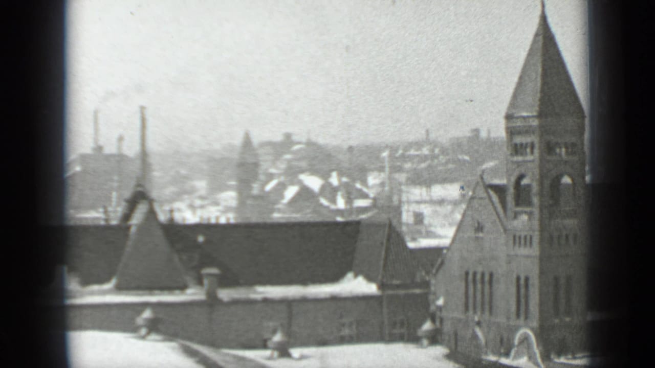 Snowy church tower and rooftops seen through dark window panes.