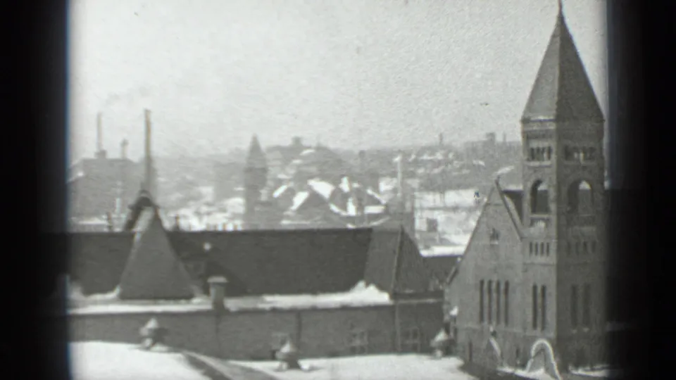 1939 New York winter view through a window, showing a snow-covered church tower, rooftops, chimneys, and distant buildings.