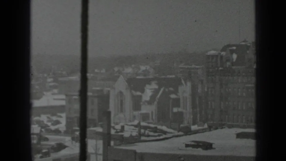 1939 New York urban winter scene with snow-covered roofs, a smaller church-like building, taller masonry buildings, and dark window framing.