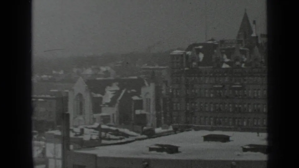 1939 New York winter city view from an elevated position, with snow-covered roofs, dark mullions, and dense buildings in haze.