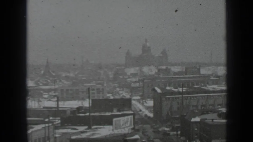 Elevated 1939 New York winter view with snowy rooftops, utility poles, a distant domed landmark, and soft film grain.