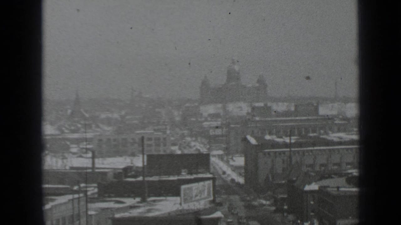 Snowy urban skyline seen from an elevated viewpoint with a distant domed building.