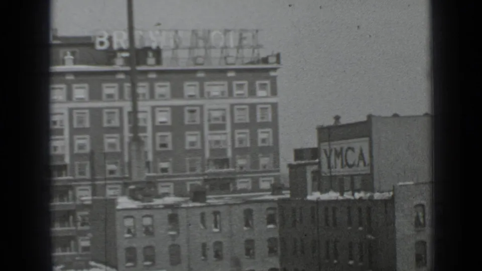 1939 New York home-movie frame concentrating on the Brown Hotel facade and adjacent YMCA sign, with snow along lower rooftops.
