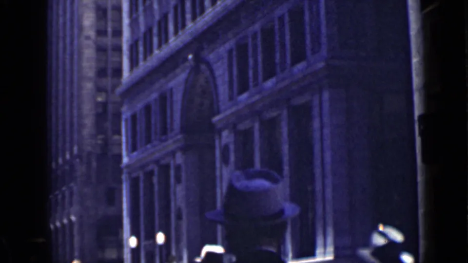 A 1939 San Francisco street-level view frames a hat-wearing pedestrian silhouette against tall masonry buildings and bright street lamps.