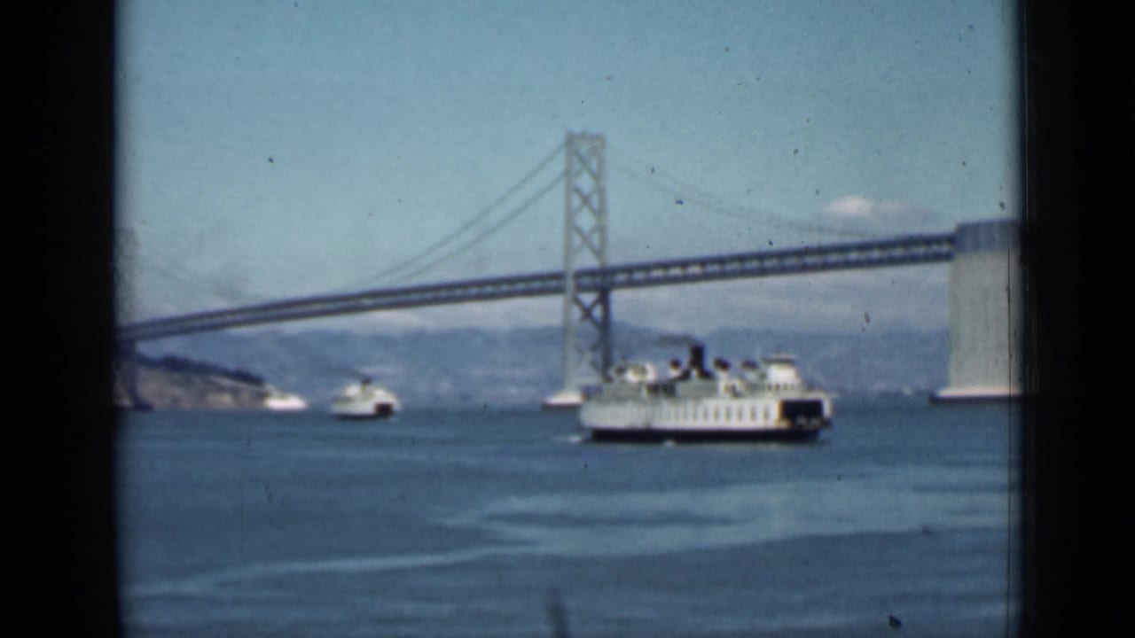 White ferry crossing San Francisco Bay near the Bay Bridge with smaller boats in the distance.