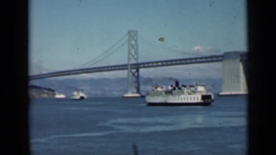 Home-movie frame from San Francisco Bay in 1939, showing a ferry beneath the Bay Bridge with small boats nearby.