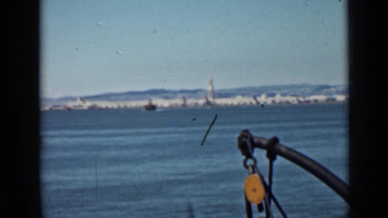 Distant San Francisco skyline across blue bay water with boat hardware in the foreground.