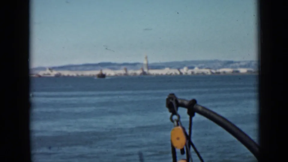 1939 home-movie frame looking across San Francisco Bay, with city buildings on the horizon and boat rigging in the foreground.