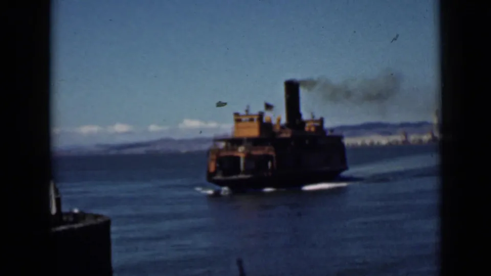 1939 San Francisco Bay frame showing a steam-powered vessel leaving a wake, with smoke rising and the shoreline in the distance.