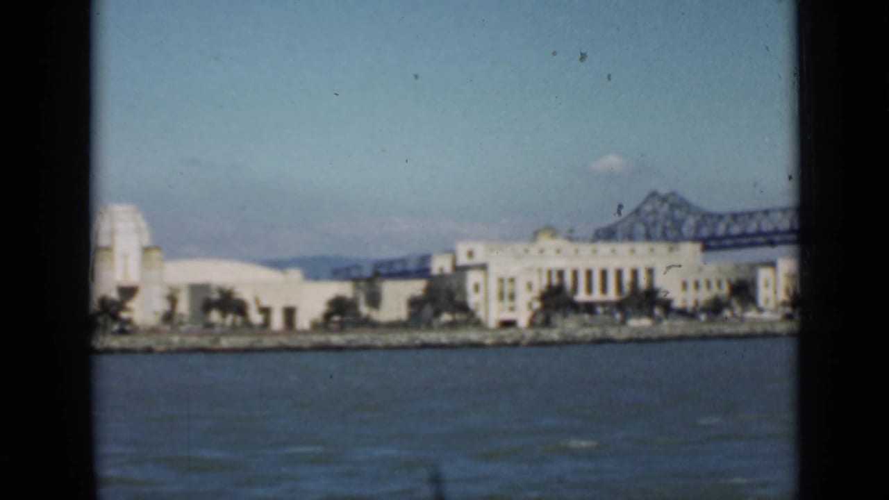 Waterfront buildings and a bridge span seen across the bay from a moving boat.