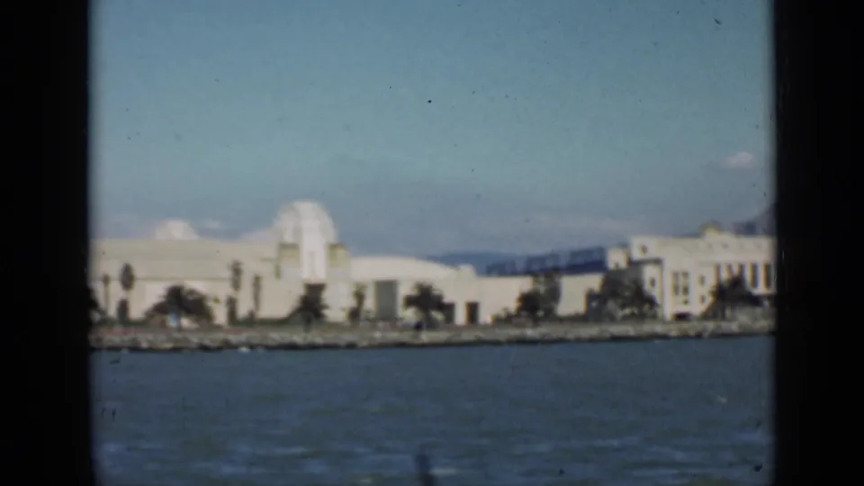 1939 boat-shot view of a white San Francisco waterfront building, shoreline plantings, and bay water.