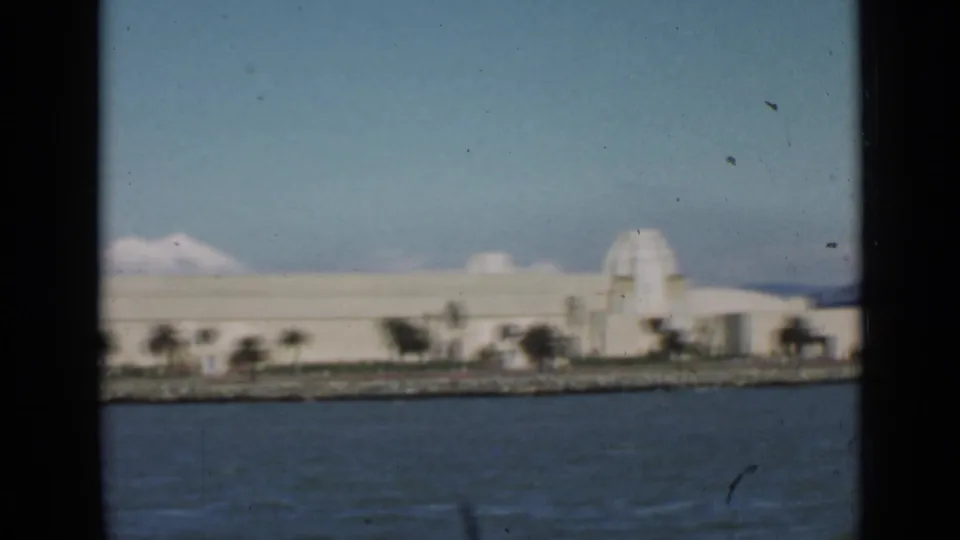 1939 San Francisco waterfront view from a boat, with bay water, a pale building, palms, and dark window edges.