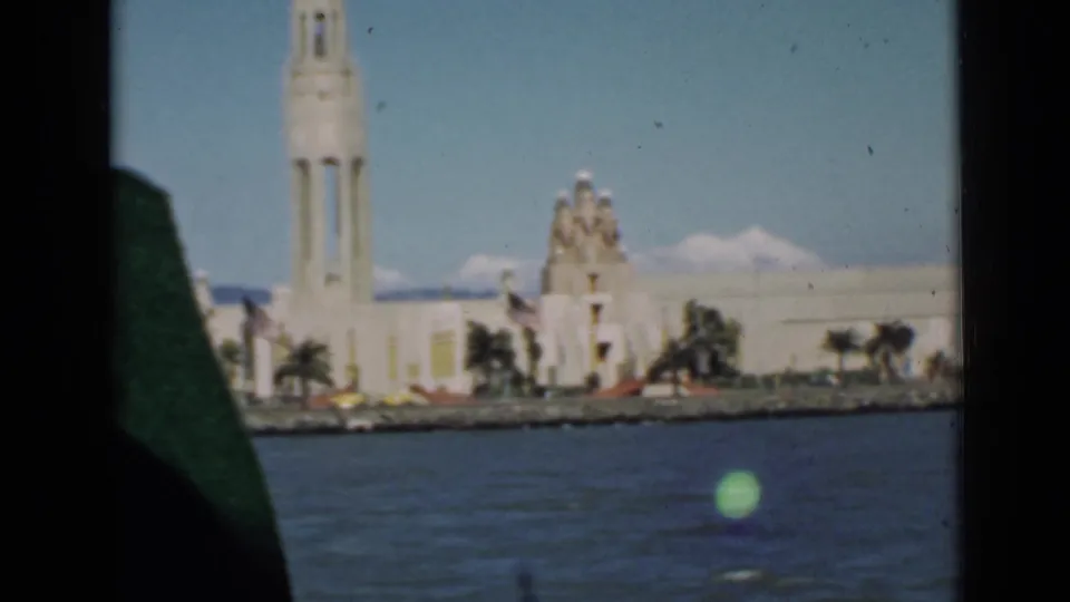 A moving 1939 boat view shows a tall waterfront tower, pale buildings, palms, and blue bay water in San Francisco.