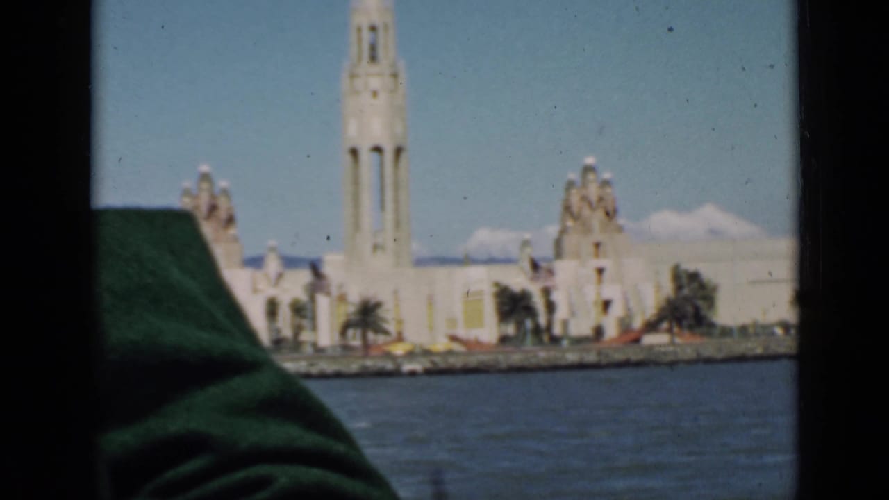 Waterfront Art Deco tower and buildings seen across blue water through a dark window frame.