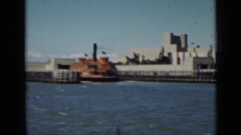 1939 San Francisco bay view showing a red-brown boat by a pier and pale exposition-era waterfront structures behind it.