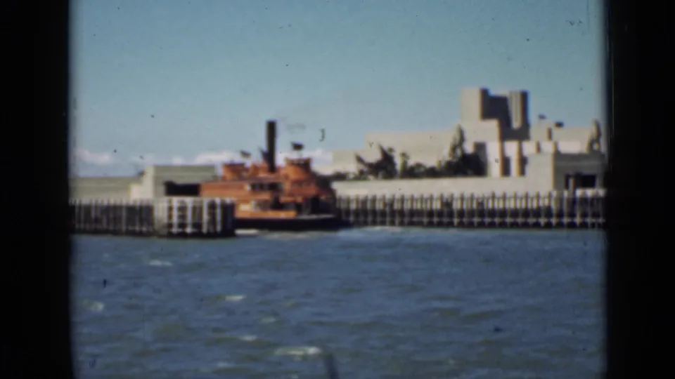 1939 San Francisco waterfront frame with a boat alongside pier railings, choppy bay water, and exposition-style buildings beyond.