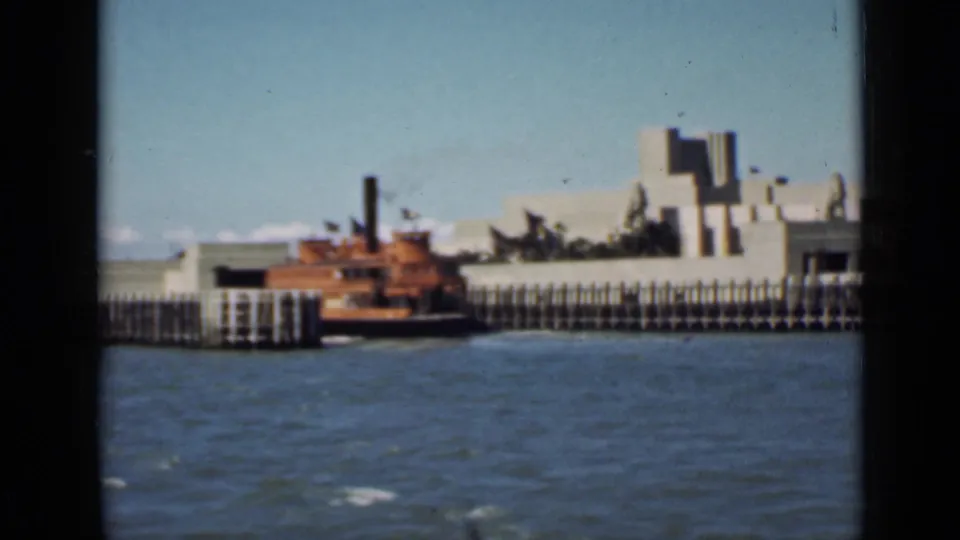 1939 San Francisco bay view with choppy water, a boat near the pier, pale Art Deco buildings, and dark window framing.