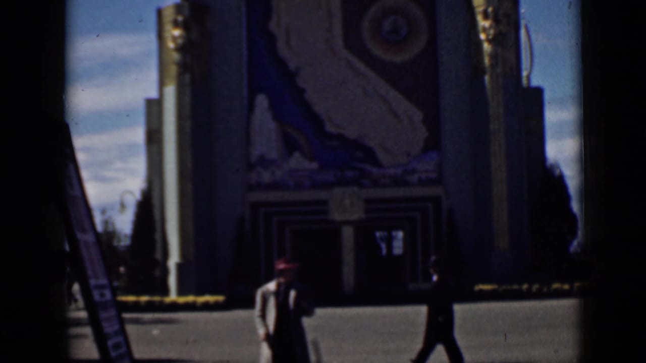 Pedestrians pass in front of a pavilion with a large California mural.