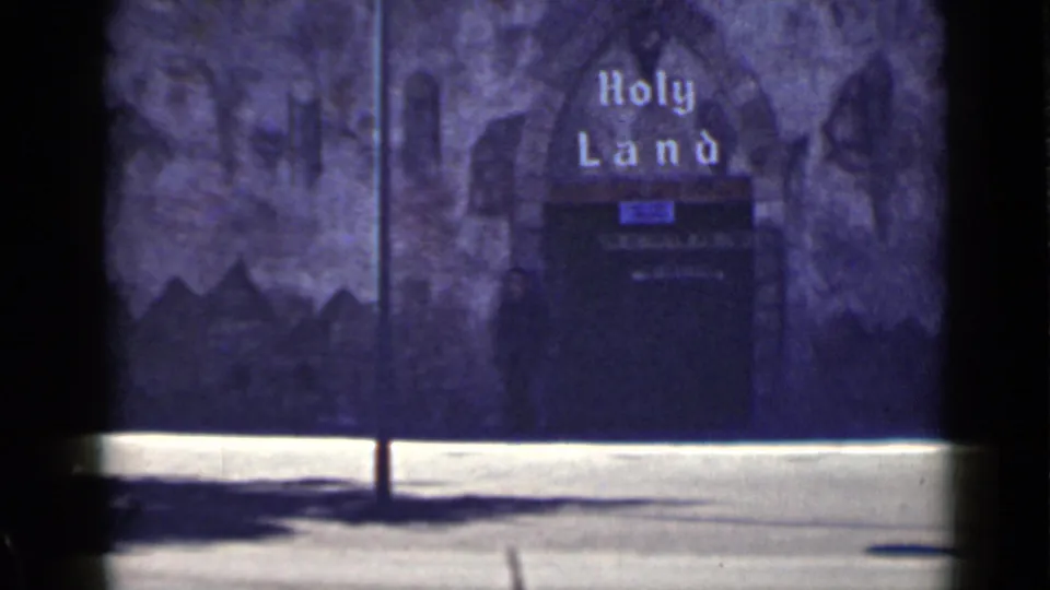 1939 San Francisco home-movie frame showing a dark facade marked Holy Land, with a shadowy figure or silhouette near the entrance.