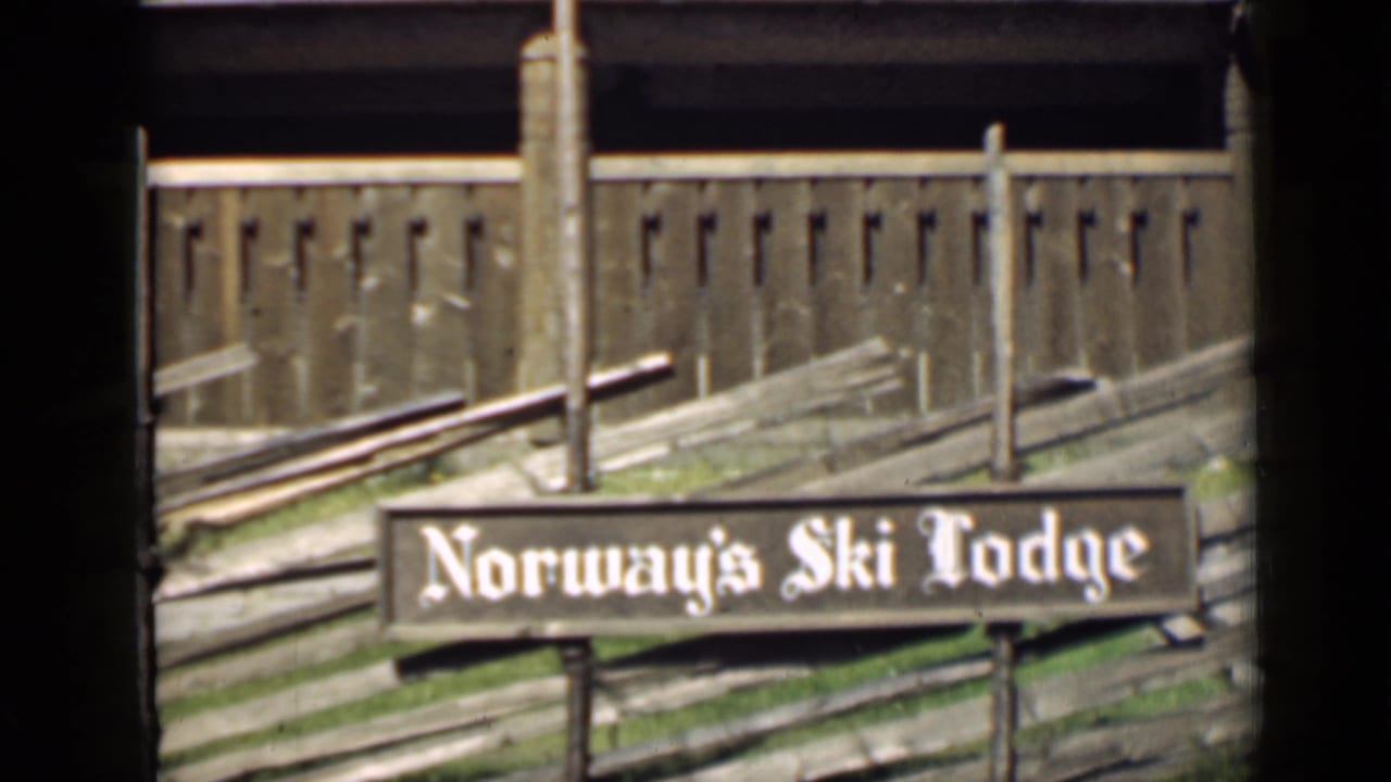 Wooden Norway’s Ski Lodge sign in front of a rustic fence and building.
