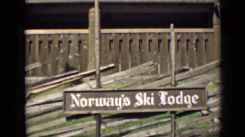 Close 8mm frame of the Norway’s Ski Lodge sign, with weathered wood fencing and lodge exterior details behind it.