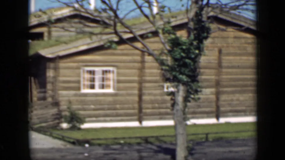 1939 San Francisco home-movie frame showing the side wall of a log building, a white-framed window, lawn, path, and ivy-covered tree.