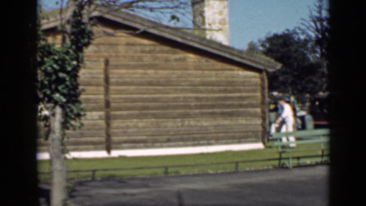 Man walking near a wooden cabin with a stone chimney and green bench.