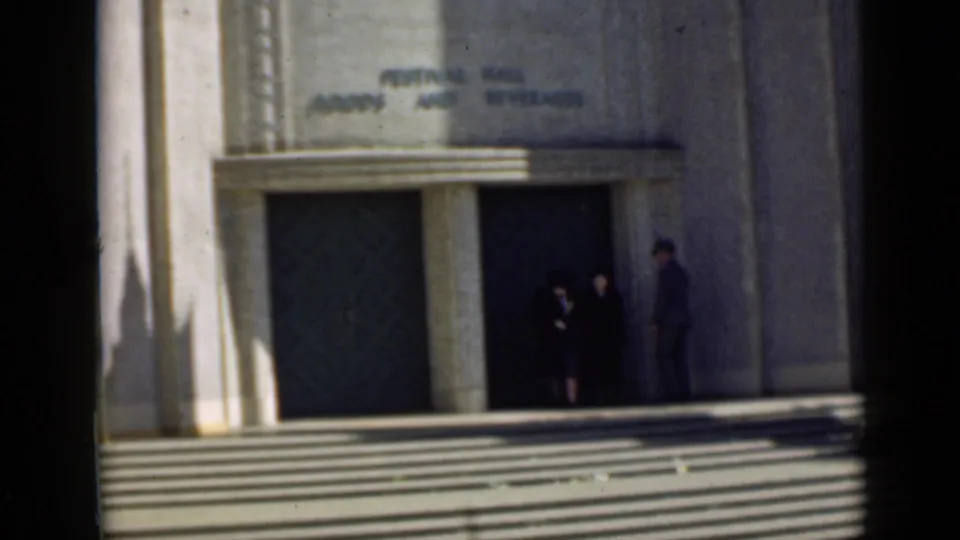 1939 San Francisco frame of visitors near a festival hall entrance with broad steps and readable wall signage.