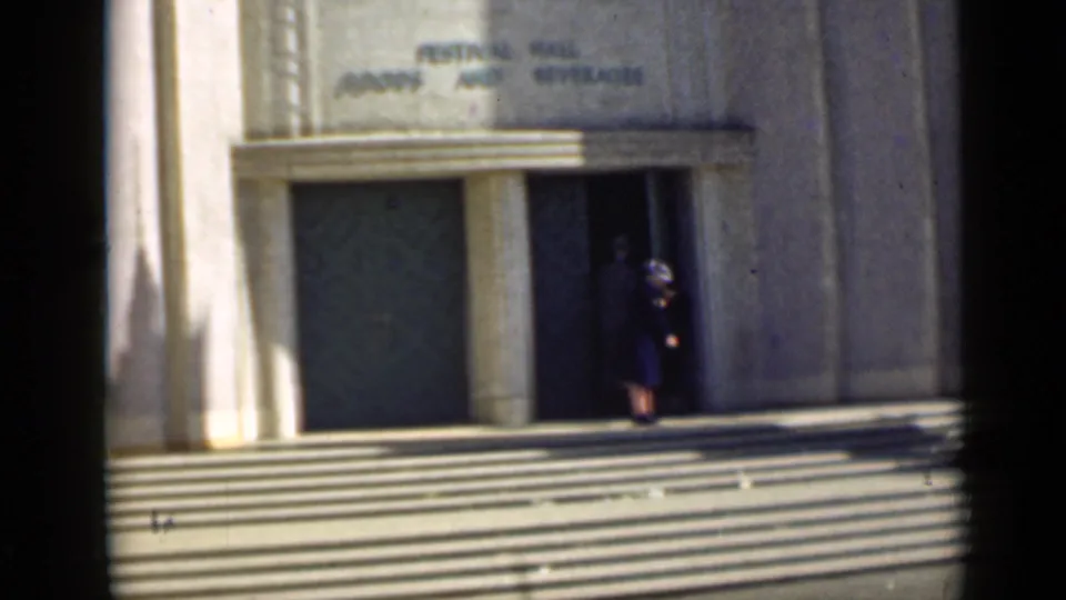 1939 San Francisco frame with a woman near festival hall steps and a blue-and-cream tour tram partly visible at right.