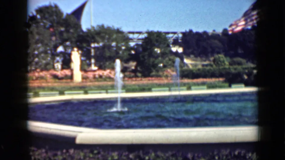 A wider San Francisco park view shows fountain jets, a statue, landscaped plantings, trees, and distant flags in 8mm color footage.
