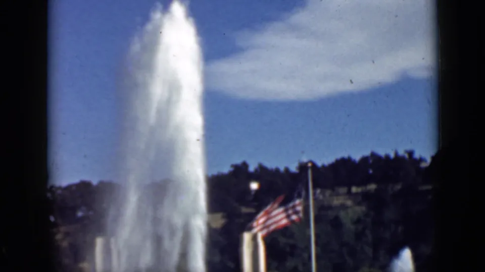 1939 San Francisco home-movie view of a tall fountain plume, nearby American flag, flagpole, and landscaped background.