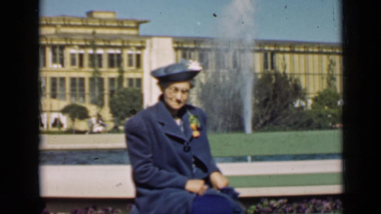Woman in blue seated on a bench with fountain spray behind her.
