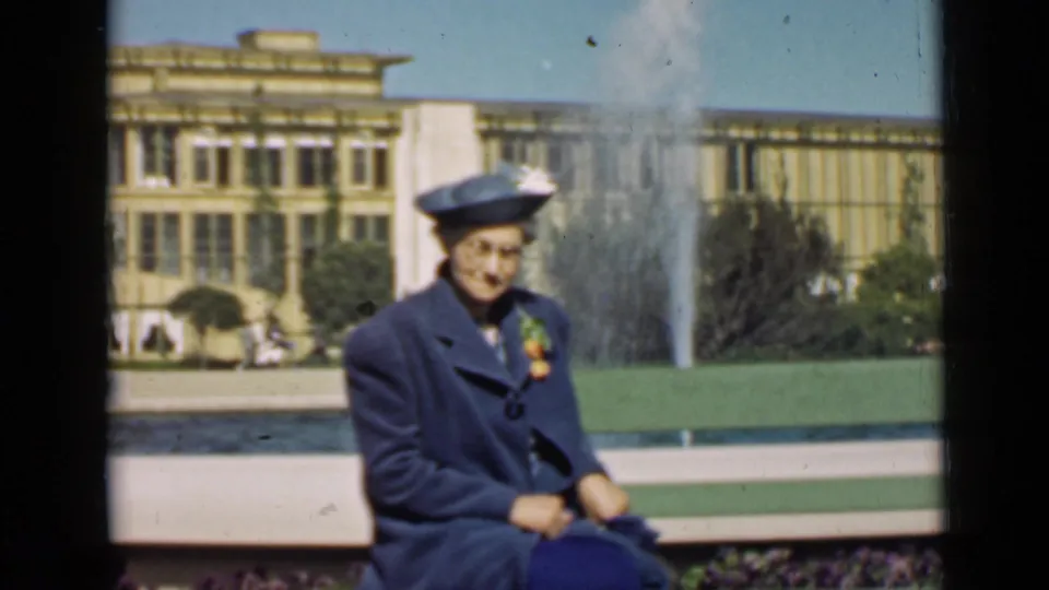 A seated woman in blue faces the camera near a fountain and formal World's Fair grounds in San Francisco.