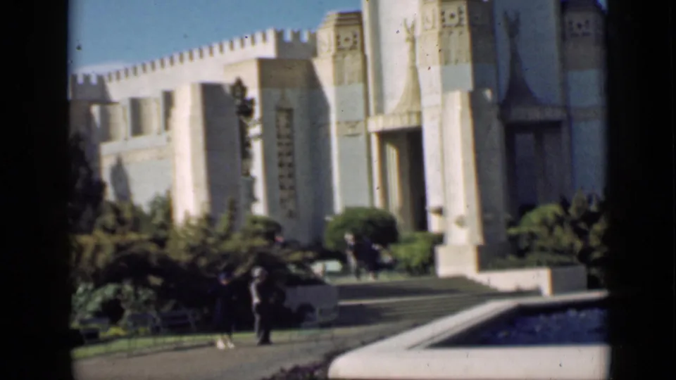 Home-movie frame showing two visitors before a pale Art Deco-style building in San Francisco, 1939.