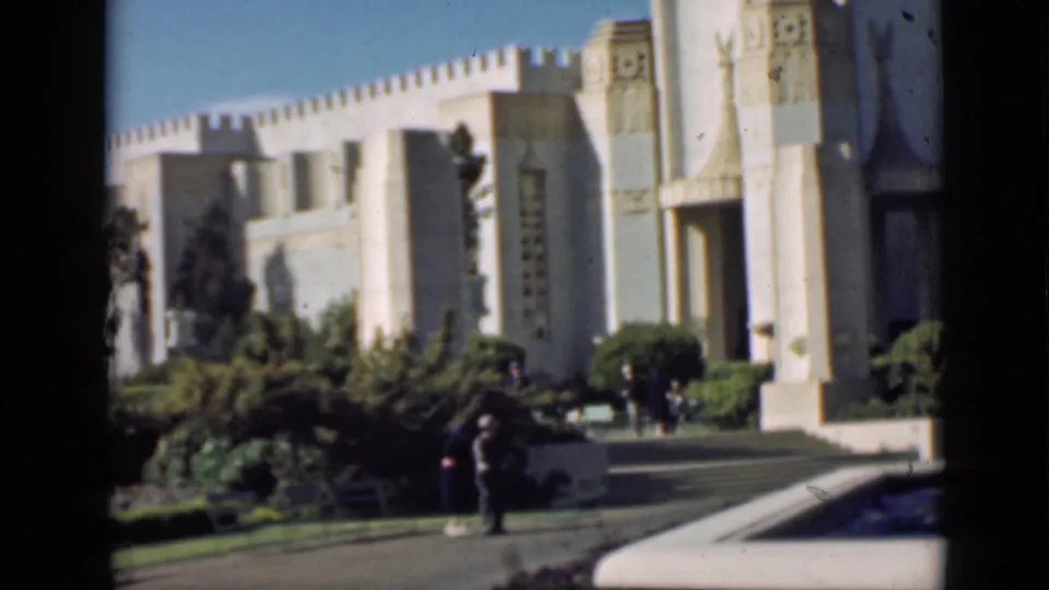1939 San Francisco frame with visitors on a path beside landscaping and an ornate public building.