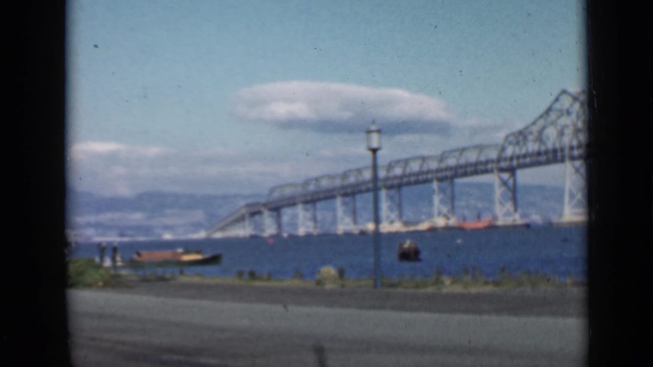 Steel truss bridge crossing blue bay water with small boats nearby.