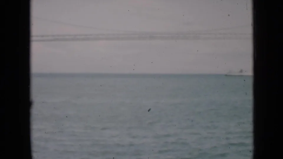 1939 San Francisco Bay home-movie frame showing a distant white ship on water, faint bridge structure, and dark window framing.