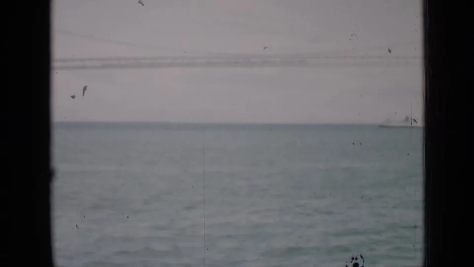 1939 San Francisco Bay frame with a small white ship near the horizon, soft overcast sky, and dark window-edge framing.