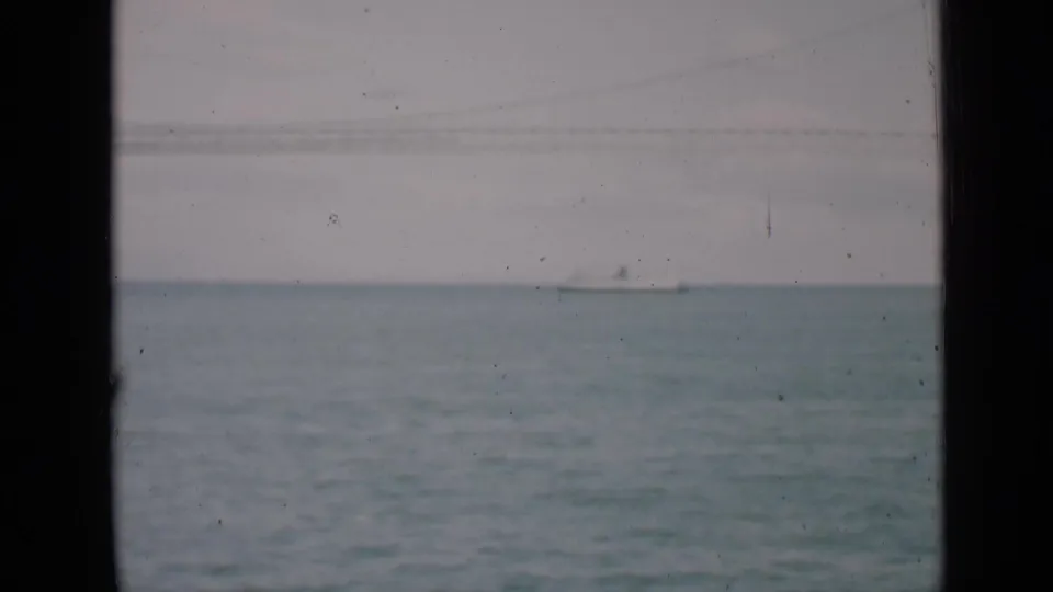 1939 San Francisco Bay home-movie frame showing a distant white ship under faint bridge lines with muted color and film grain.