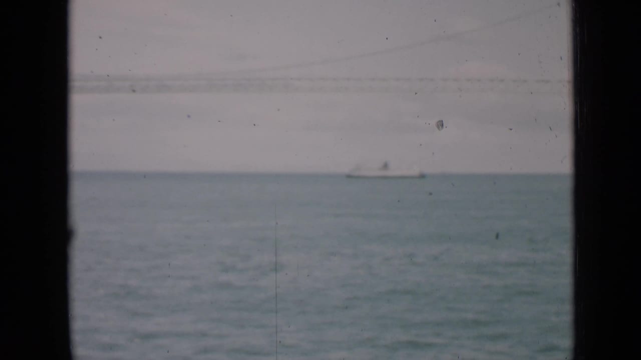 Distant sailboat on blue-gray water seen through dark vertical window frames.