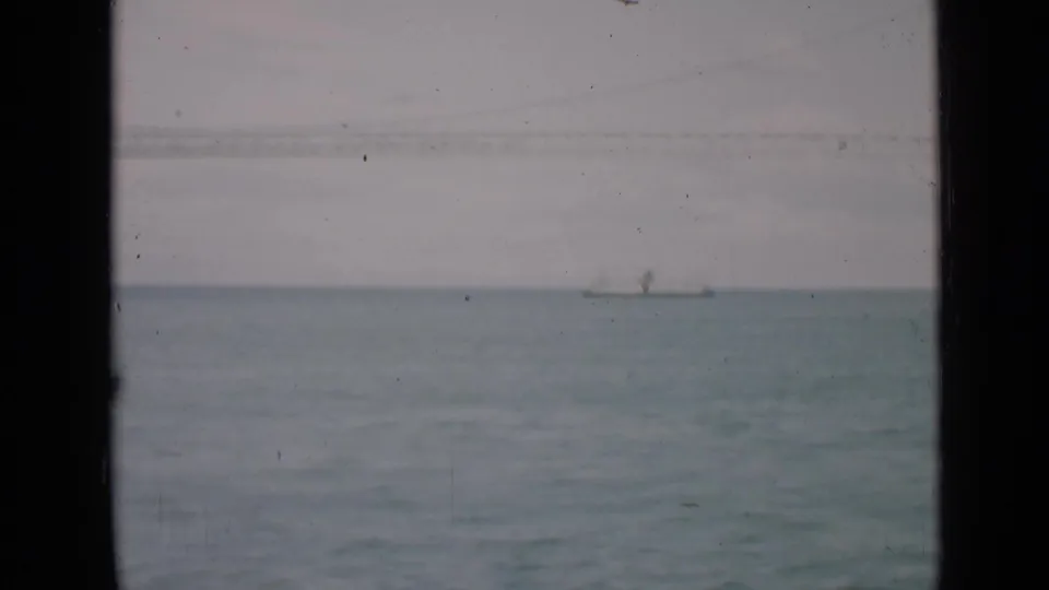 Distant sailboat on San Francisco water in a soft 1939 8mm frame, with dark vertical framing and visible film specks.