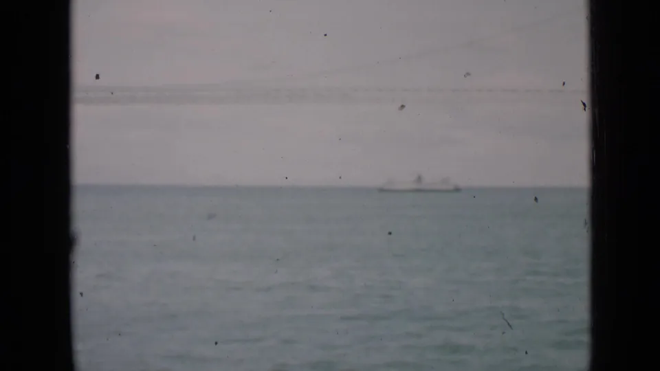 1939 San Francisco bay view with a distant boat and faint bridge span, seen through dark foreground framing on 8mm film.