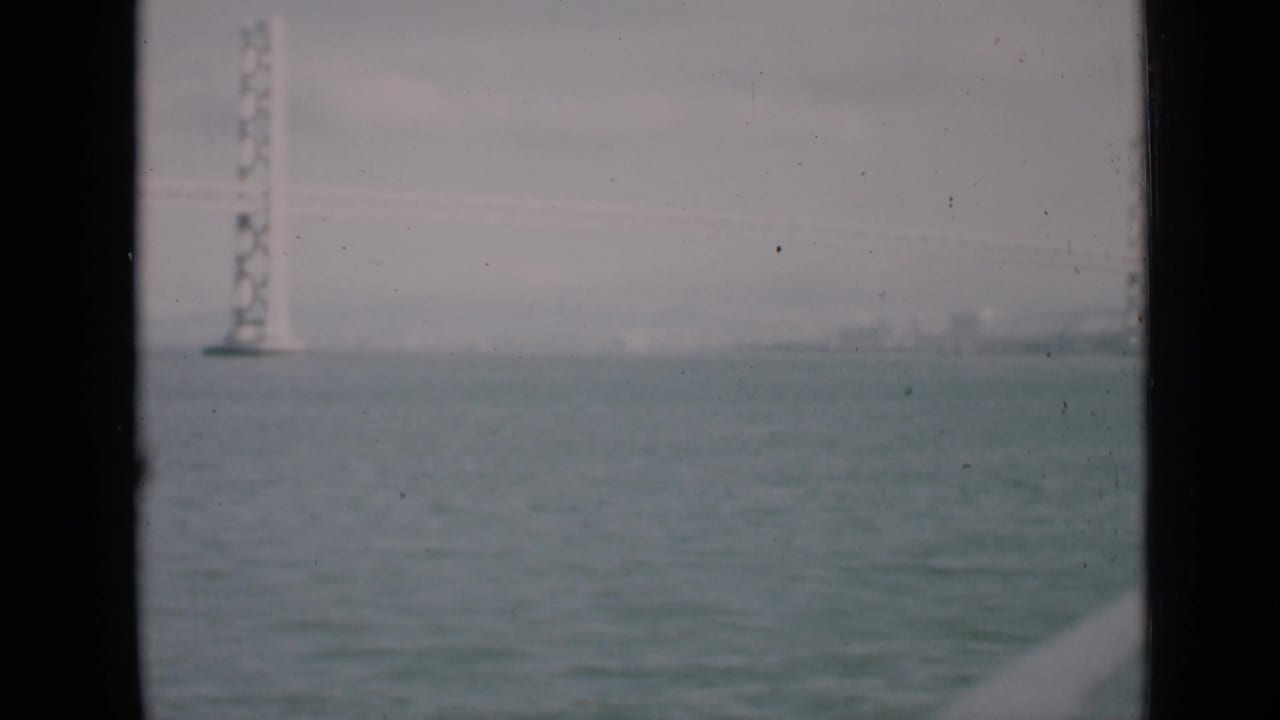 Hazy bay water with a distant suspension bridge tower and dark vertical framing.