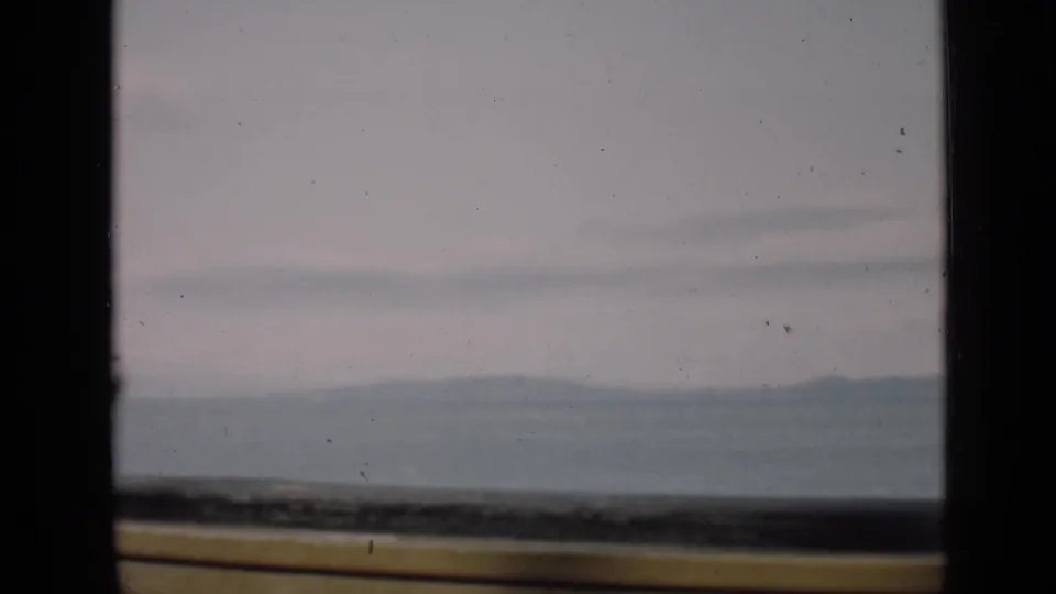 1939 San Francisco home-movie frame showing a fog-muted distant landscape through dark window mullions and a yellow lower ledge.
