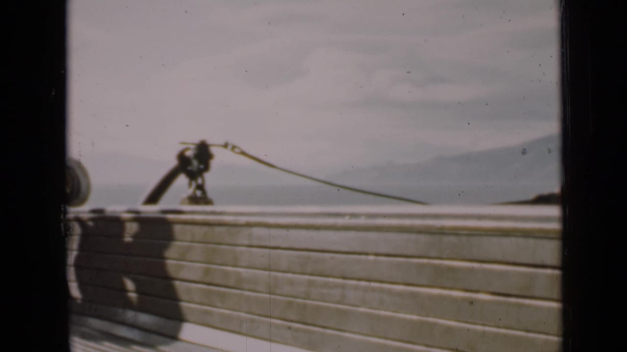Wooden boat railing with a deck fitting and rope line against water and hills.